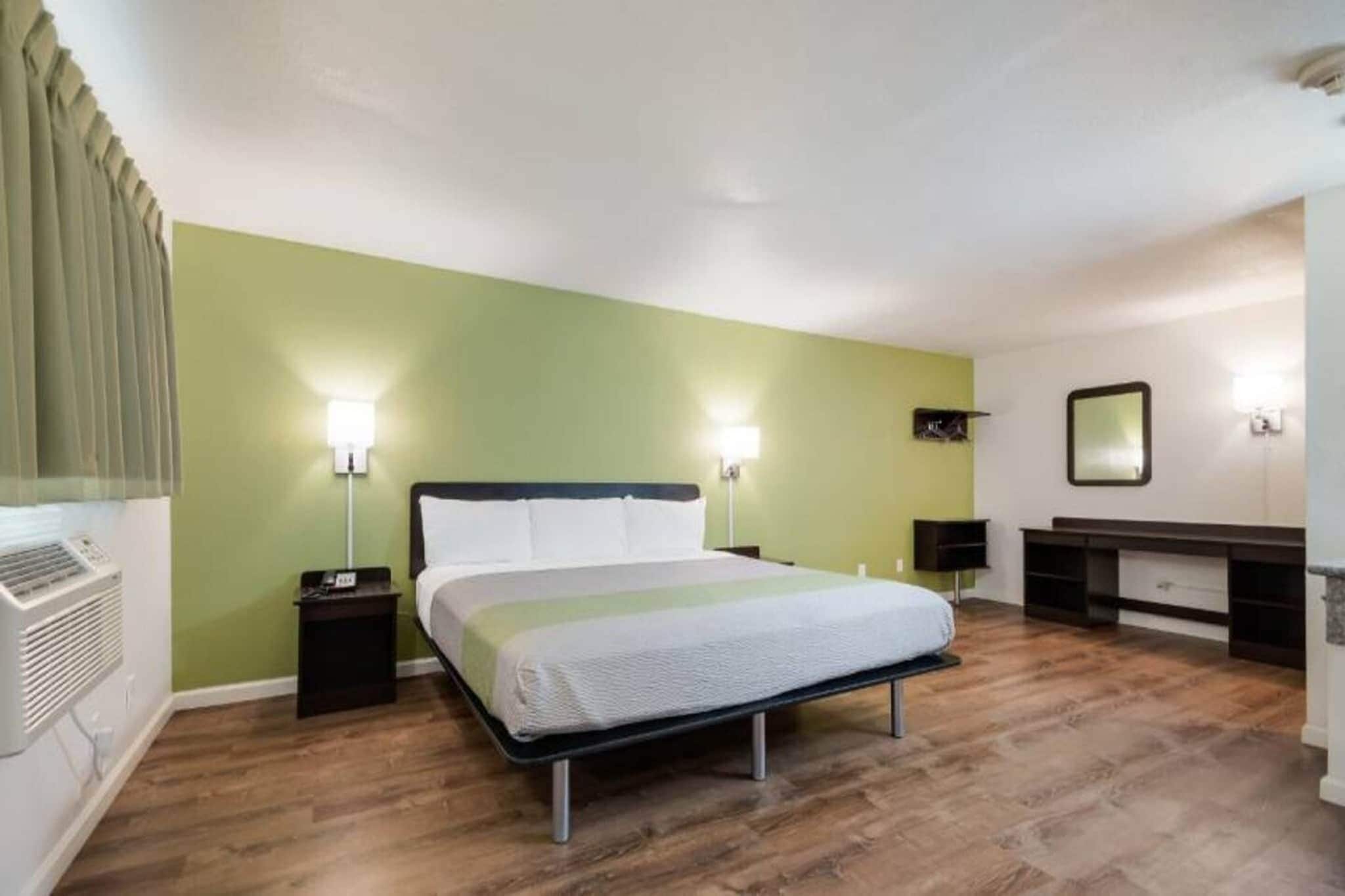 Quarto com cama, mesas de cabeceira, espelho e aquecedor fixado na parede.