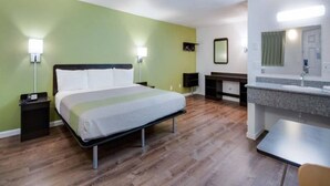 Habitación de hotel con cama, mesitas de noche, escritorio, espejo y baño con lavamanos y espejo.