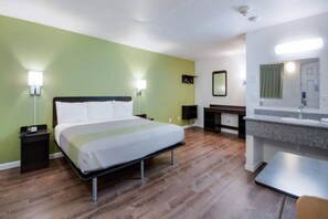 Quarto de hotel com cama, mesas de cabeceira, escrivaninha, espelho e banheiro com pia e espelho.
