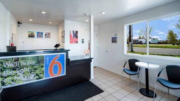 A hotel reception area with a reception desk, two chairs, a window with a view of the outside, and a tiled floor.
