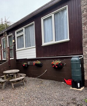 A wooden building with large windows, a wooden bench, and flower planters. - Two-Bedroom Chalet at Penstowe Park, Near Bude Beaches (Kilkhampton)