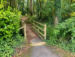 A wooden footbridge in a forested area with a paved path leading through it. - Two-Bedroom Chalet at Penstowe Park, Near Bude Beaches (Kilkhampton)