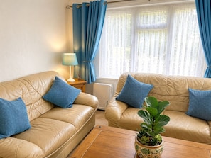 A living room with two beige leather sofas, blue cushions, a wooden coffee table, a floor lamp, and a potted plant. - Two-Bedroom Chalet at Penstowe Park, Near Bude Beaches (Kilkhampton)