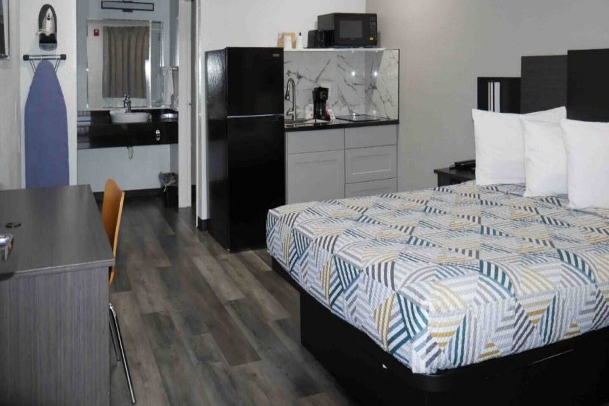 A hotel room with a bed, a desk, a chair, a kitchenette, and a bathroom.
