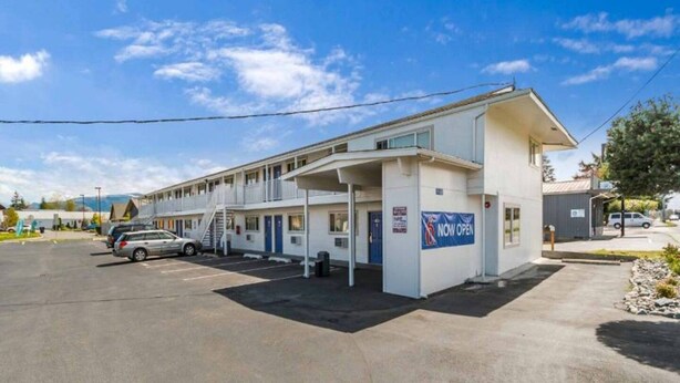 Un motel con una estructura de dos pisos, un área de estacionamiento techada y un letrero que indica que está abierto.