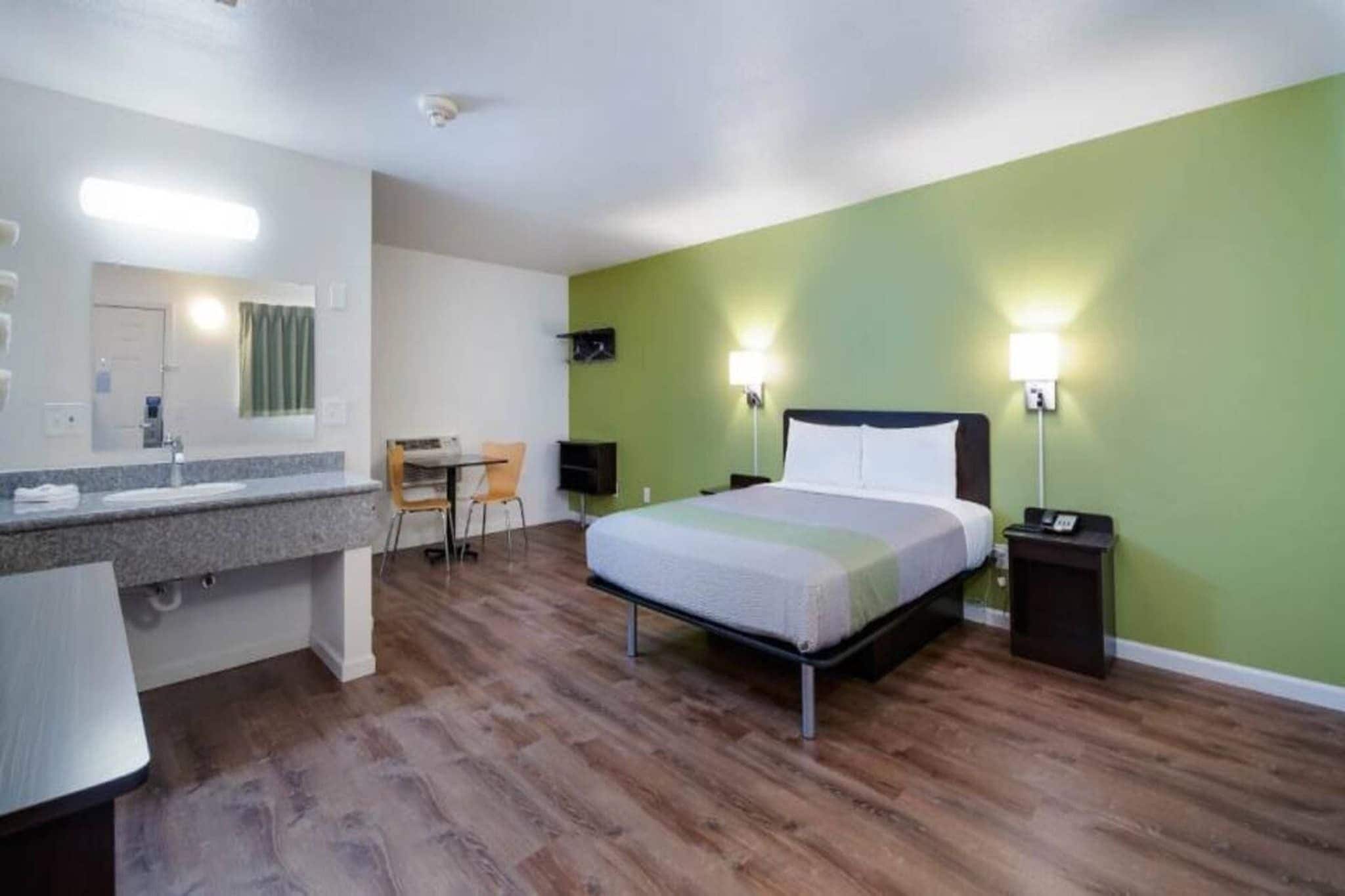 Habitación de hotel con cama, escritorio, silla, tocador con espejo y mesita de noche.