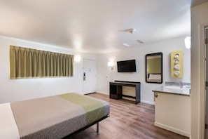 Quarto de hotel com cama, escrivaninha, espelho e televisão.