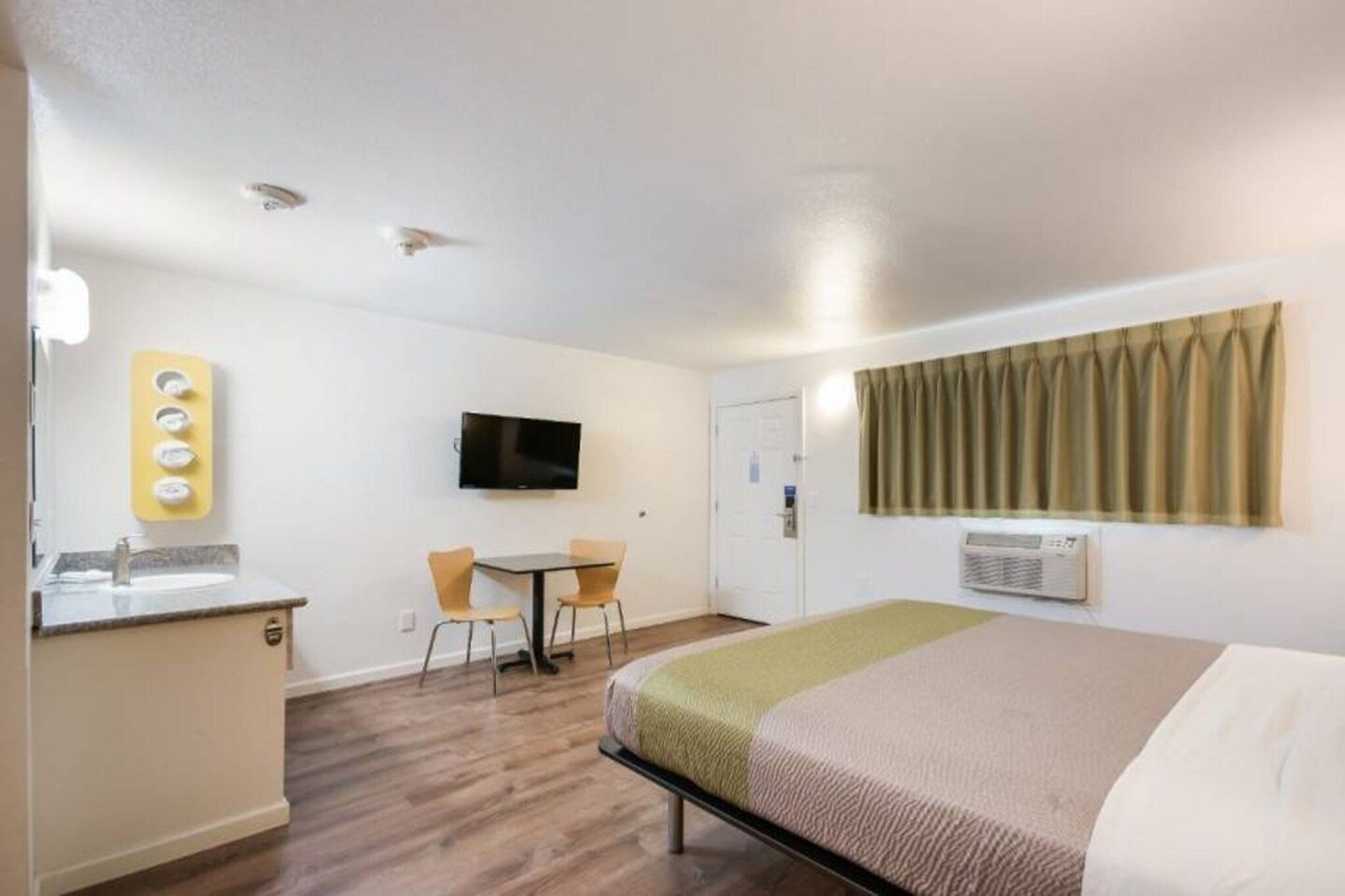 Quarto de hotel com cama, escrivaninha com cadeira, televisão e banheiro.