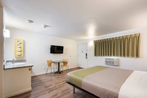 A hotel room with a bed, a desk with a chair, a television, and a bathroom.