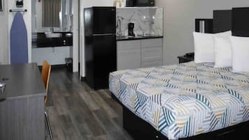 A hotel room with a bed, a desk, a chair, a kitchenette, and a bathroom.