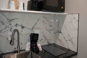 A kitchen with a stainless steel sink, a black coffee maker, a microwave, and a marble backsplash.