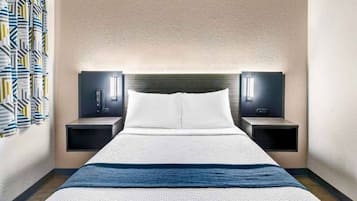 Hotellihuone, jossa on sänky, kaksi yöpöytää, sängynpääty ja seinään kiinnitetty valaisin.