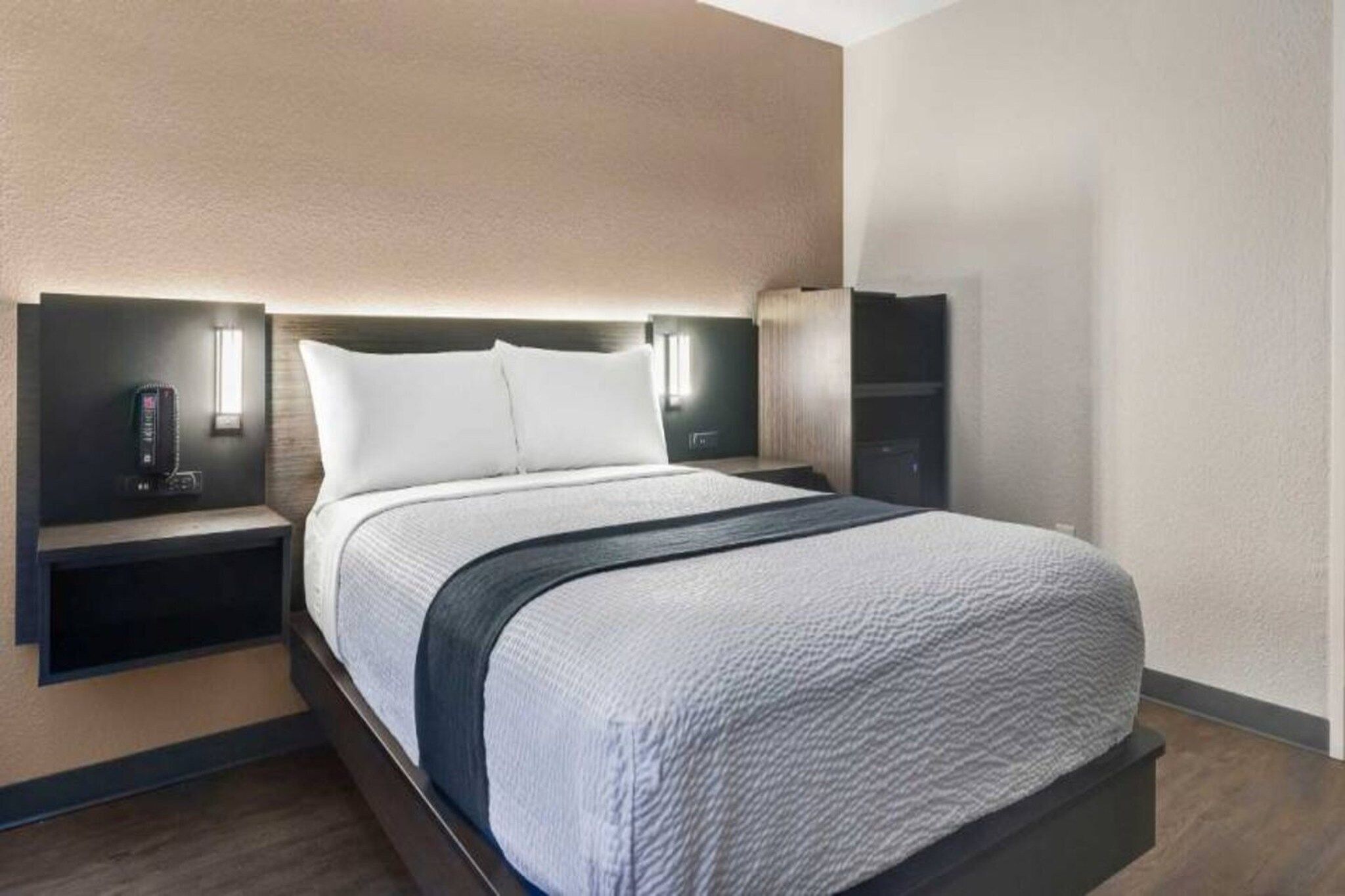 Una habitación de hotel moderna con una cama grande, mesitas de noche e iluminación integrada en la pared.