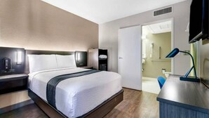 A modern hotel room with a large bed, bedside tables, a desk, and a bathroom visible through an open door. - 1 Queen Bed | Deluxe (Issaquah)