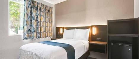 A hotel room with a bed, bedside tables, a wardrobe, and a window with patterned curtains.