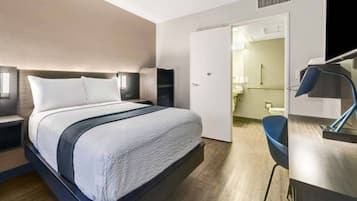 Moderni hotellihuone, jossa on suuri sänky, yöpöydät, työpöytä ja kylpyhuone, joka näkyy avoimesta ovesta.