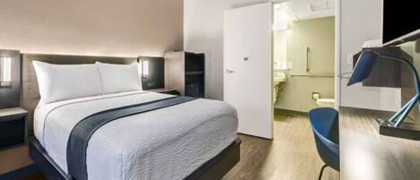 A modern hotel room with a large bed, bedside tables, a desk, and a bathroom visible through an open door.