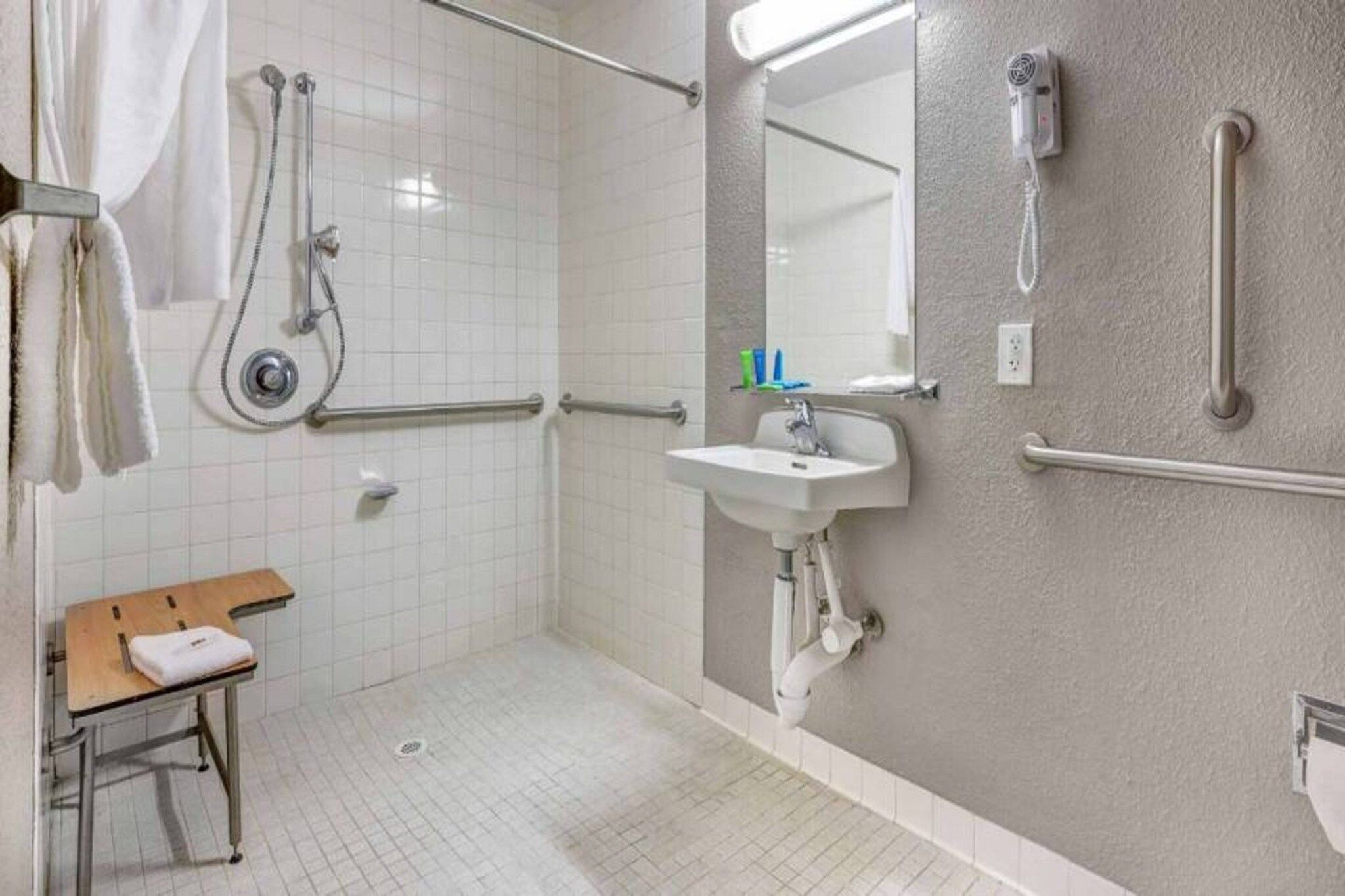Ein Badezimmer mit Dusche, Haltegriffen, Waschbecken und Handtuchhalter.