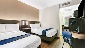 Ein Hotelzimmer mit zwei Betten, einem Schreibtisch mit Stuhl und einem durchgehenden Türbogen einsehbarer Badezimmer.