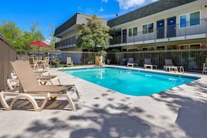 A swimming pool with lounge chairs and a building with balconies. - 2 Full Beds | Deluxe (Issaquah)