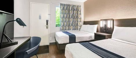 A hotel room with a bed, bedside table, lamp, chair, and a patterned curtain.