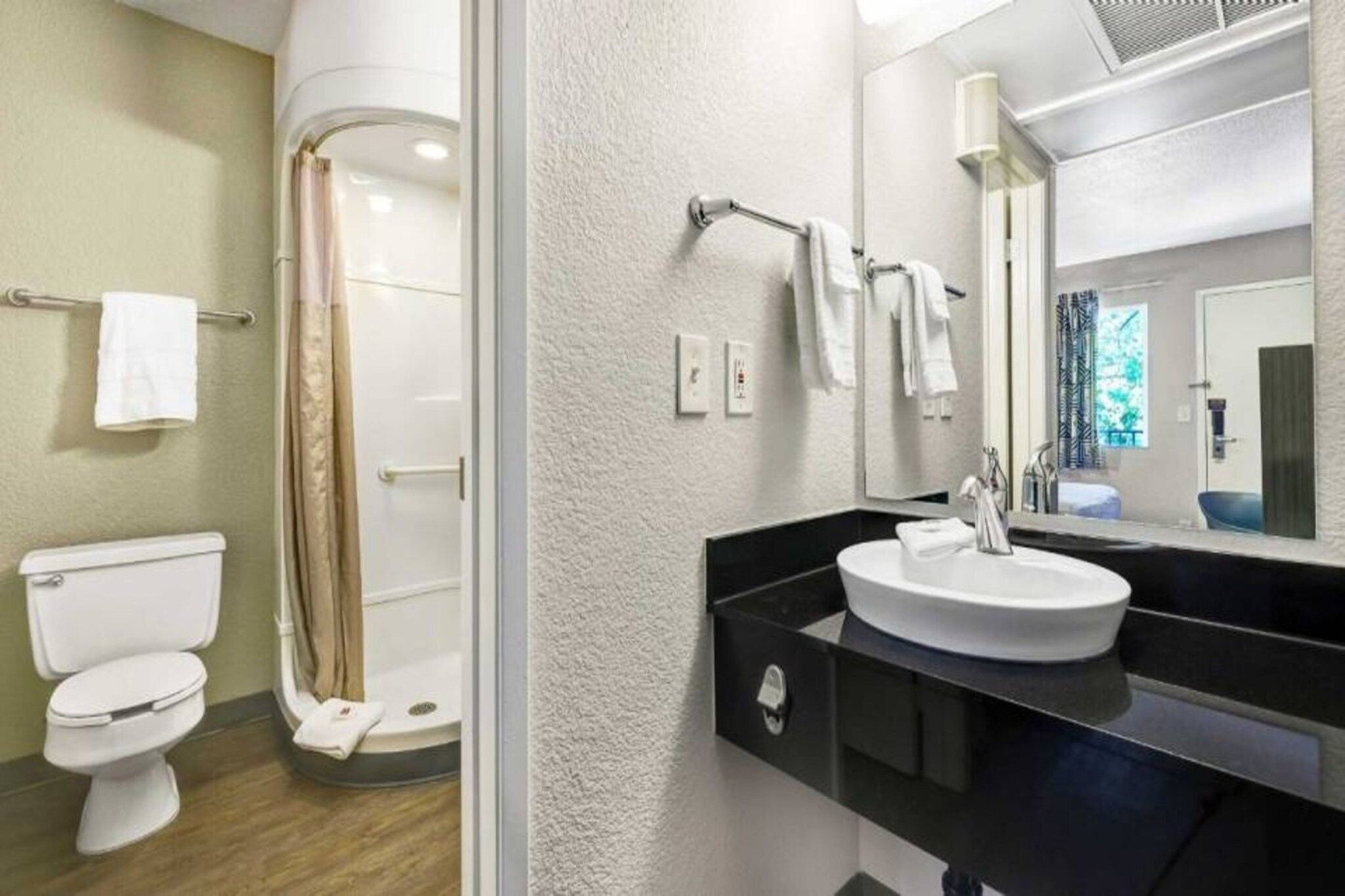 A bathroom with a toilet, shower, sink, and mirror.