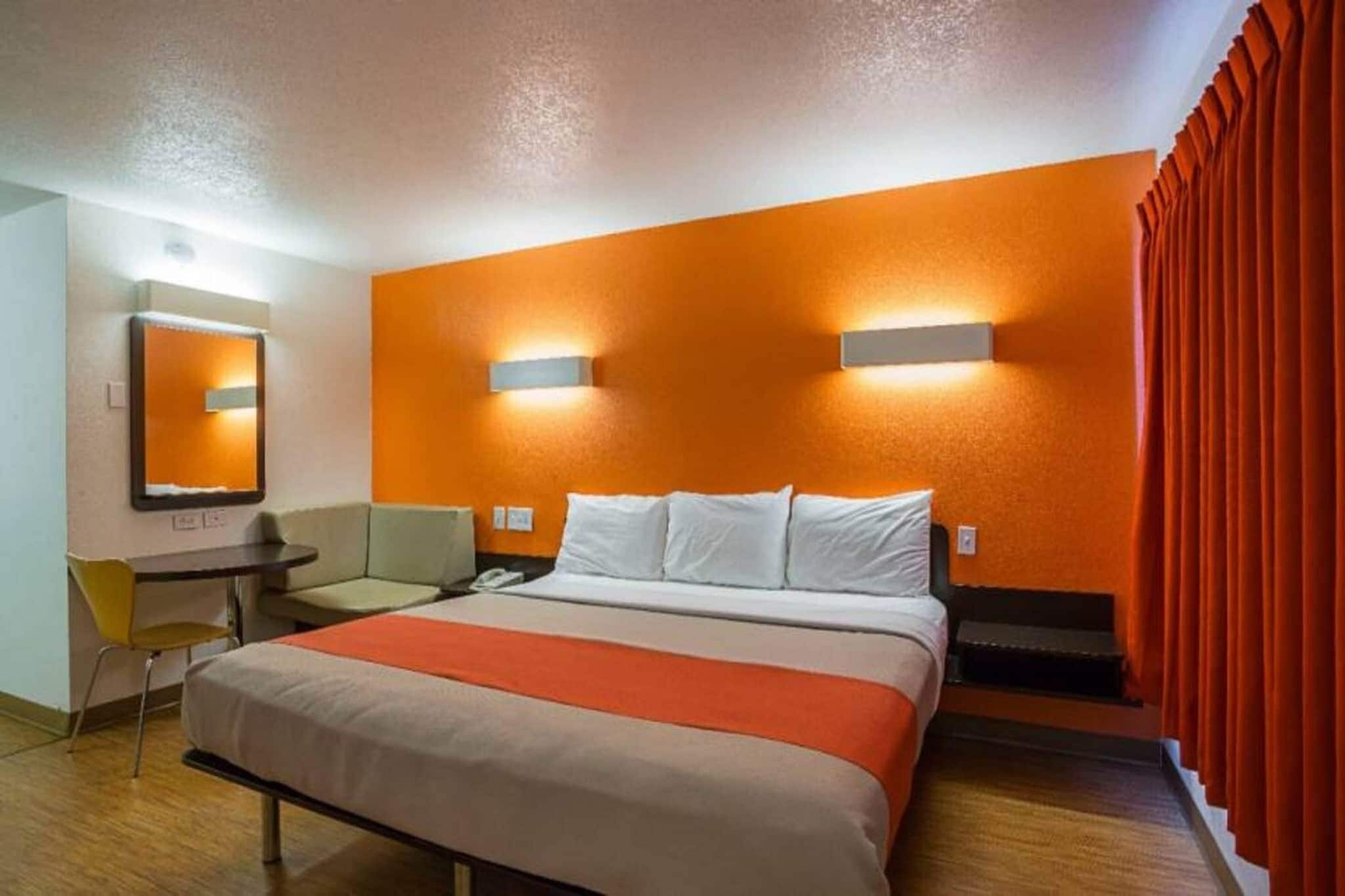 A hotel room with a bed, a desk, a chair, and a mirror.