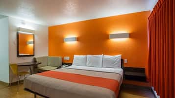 A hotel room with a bed, a desk, a chair, and a mirror.
