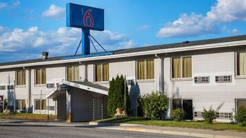 A hotel with a prominent blue sign with the number 6, a covered entrance, and a parking lot in front.