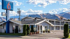 Un motel avec une grande enseigne, un parking et des montagnes en arrière-plan.