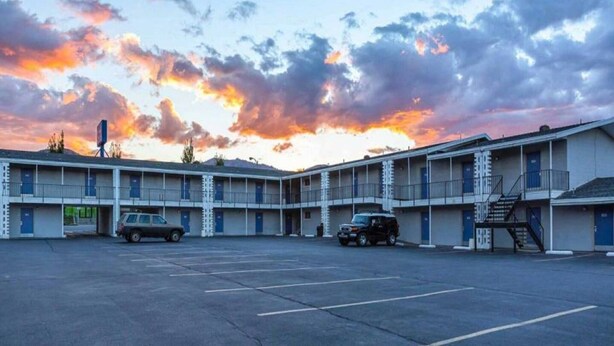 Un motel à plusieurs étages, un parking et un ciel au coucher du soleil.