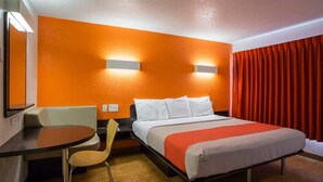Une chambre d’hôtel avec un lit, un bureau, une chaise et un rideau rouge.