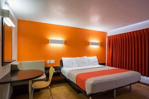 Habitación de hotel con cama, escritorio, silla y cortina roja.