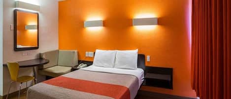 A hotel room with a bed, a desk, a chair, and a mirror.