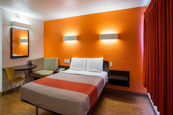 A hotel room with a bed, a desk, a chair, and a mirror.