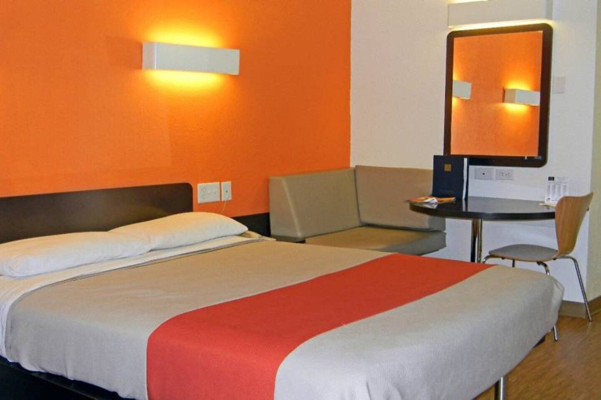 Habitació d'hotel amb llit, escriptori, cadira i un gran mirall.