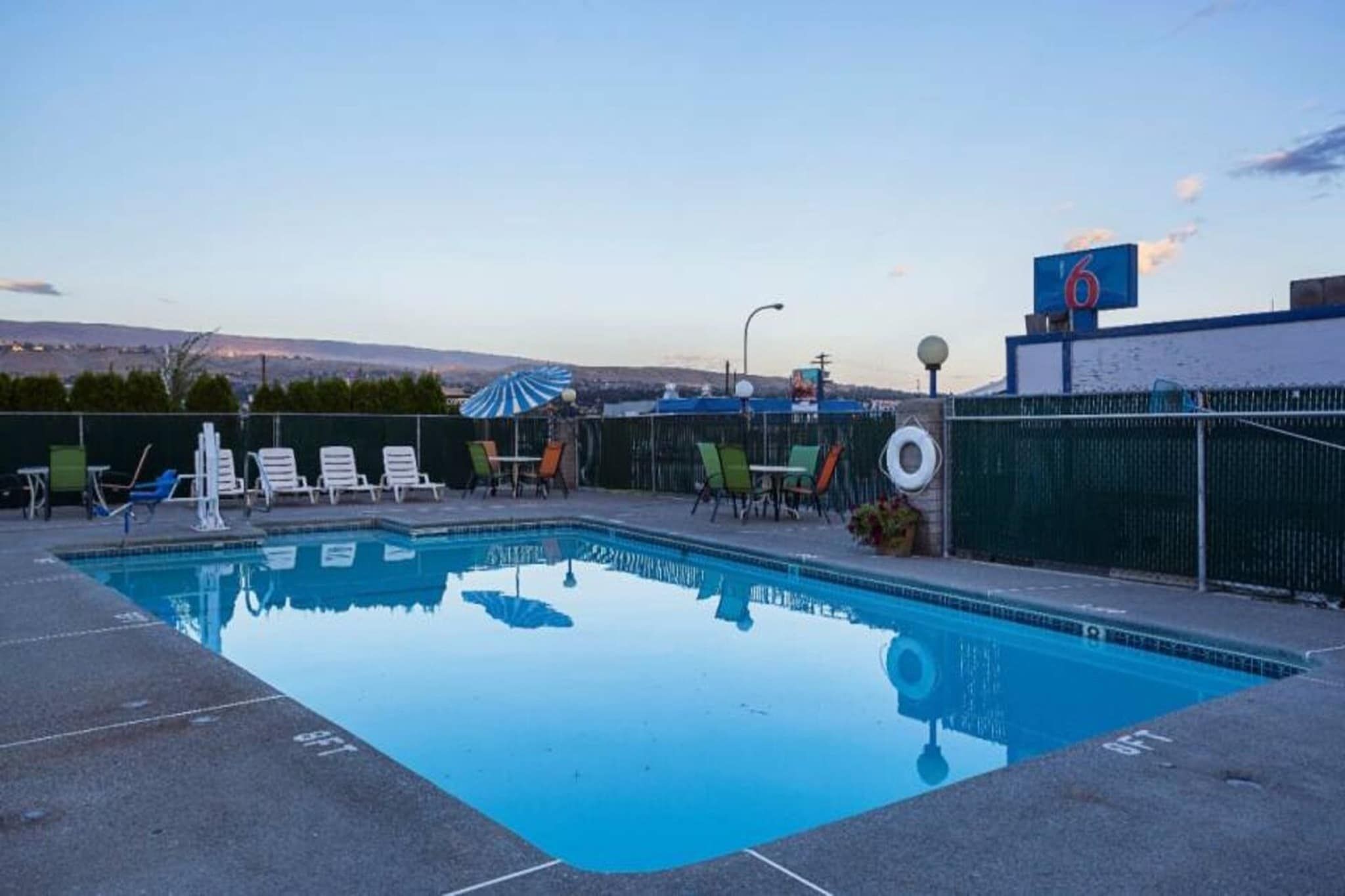 A swimming pool with lounge chairs and umbrellas, surrounded by a fence.