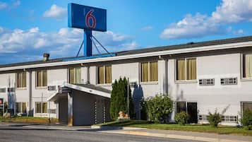 A hotel with a prominent blue sign with the number 6, a covered entrance, and a parking lot in front.