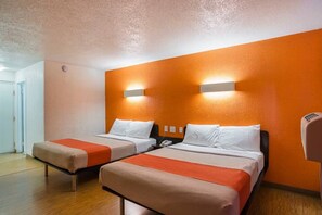 Una habitación de hotel con dos camas, suelo de madera y una lámpara fijada a la pared.