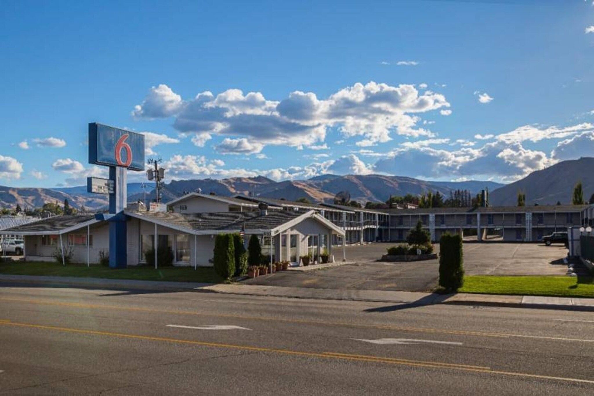 A motel with a large sign, a parking lot, and mountains in the background.