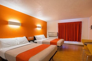 Habitación de hotel con dos camas, una mesita pequeña, una silla y un ventanal con cortinas.