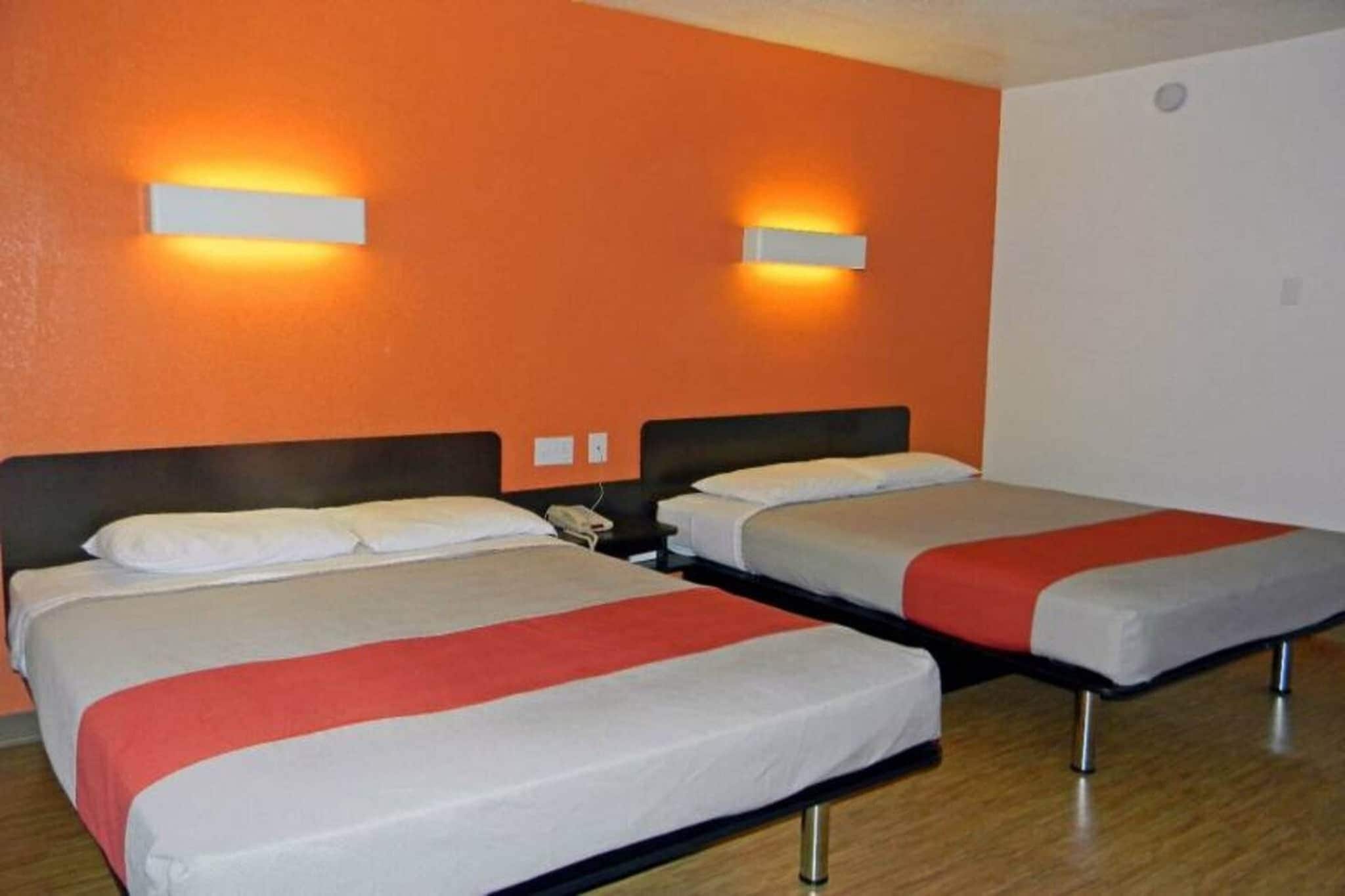 A hotel room with two beds, each with a white and red bedspread, and two wall-mounted light fixtures.