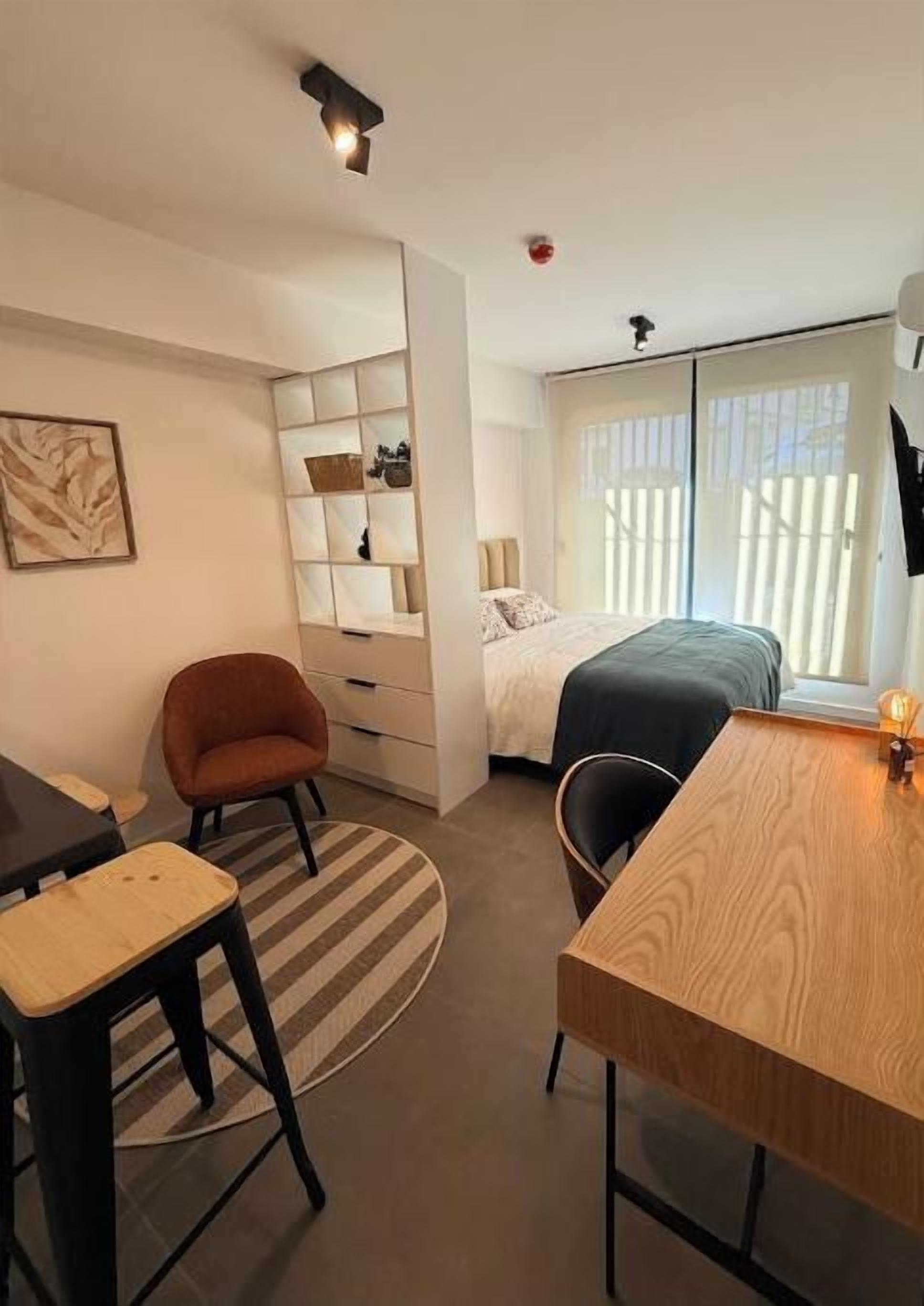 A compact room with a bed, a desk, a chair, and a built-in shelving unit.