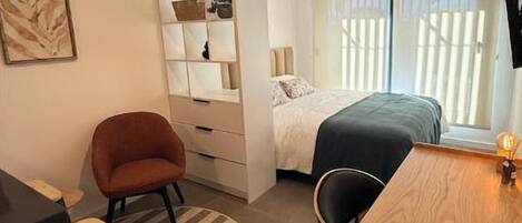 A compact room with a bed, a desk, a chair, and a built-in shelving unit.