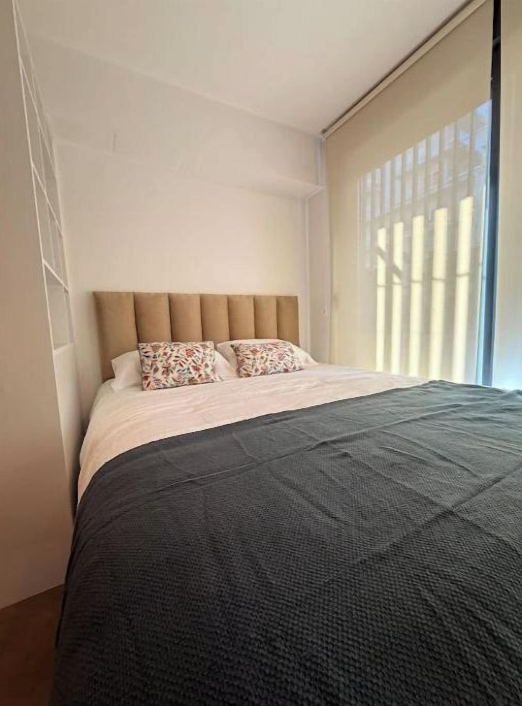 A bedroom with a bed, a headboard, and a window with blinds.