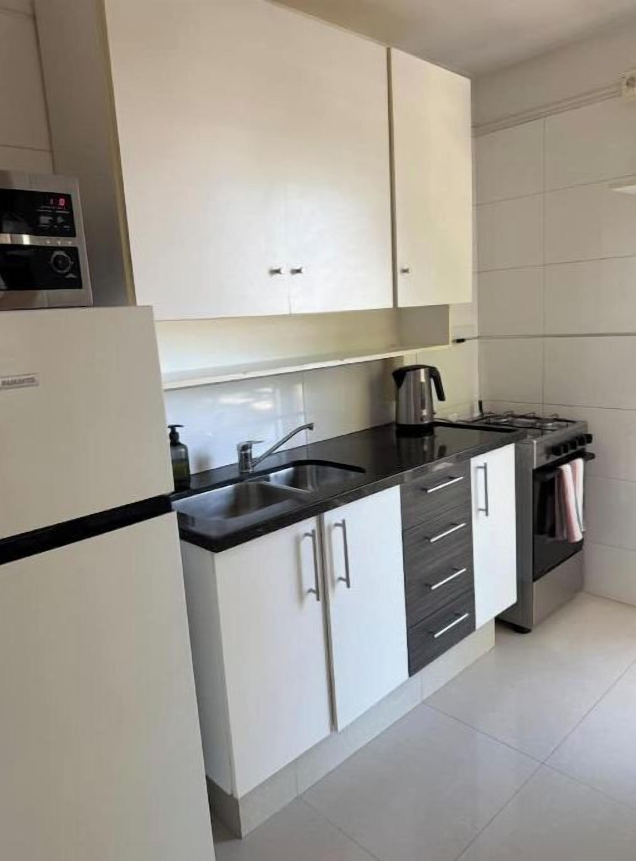 Una cucina con mobili bianchi, un piano di lavoro nero, un forno a microonde, un bollitore e un fornello.