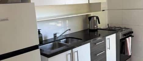 A kitchen with white cabinets, a black countertop, a microwave, a kettle, and a stove.