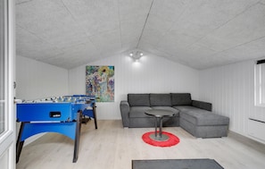 Ein Zimmer mit einem Kicker, einem grauen Ecksofa und einem roten Teppich.