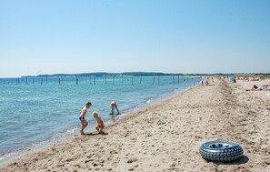 Ein Strand mit klarem Wasser, Menschen die entlanggehen und einem Reifen im Sand.
