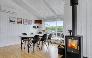 Ein modernes Interieur mit Essbereich, weißen Wandverkleidungen, einem großen Fenster und einem Kaminofen.